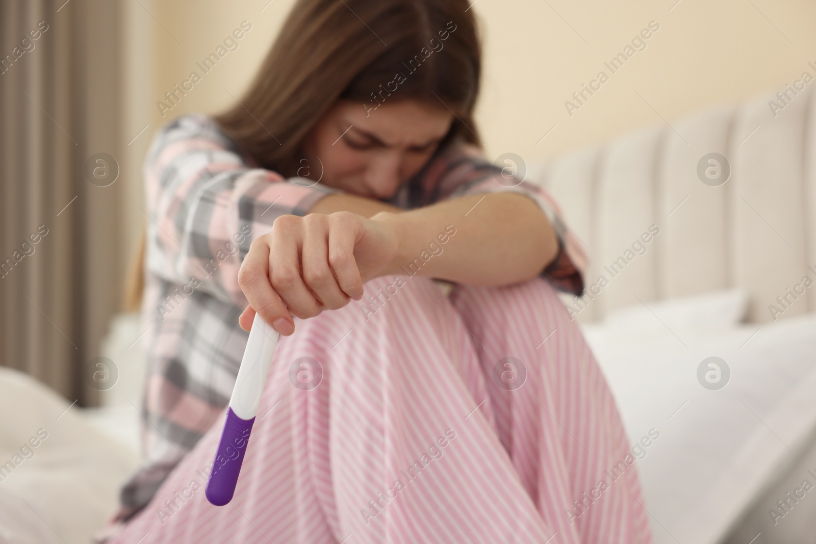 Photo of Upset woman with negative pregnancy test on bed at home, selective focus