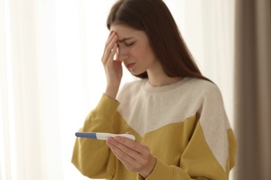 Photo of Upset woman with negative pregnancy test near window at home, selective focus