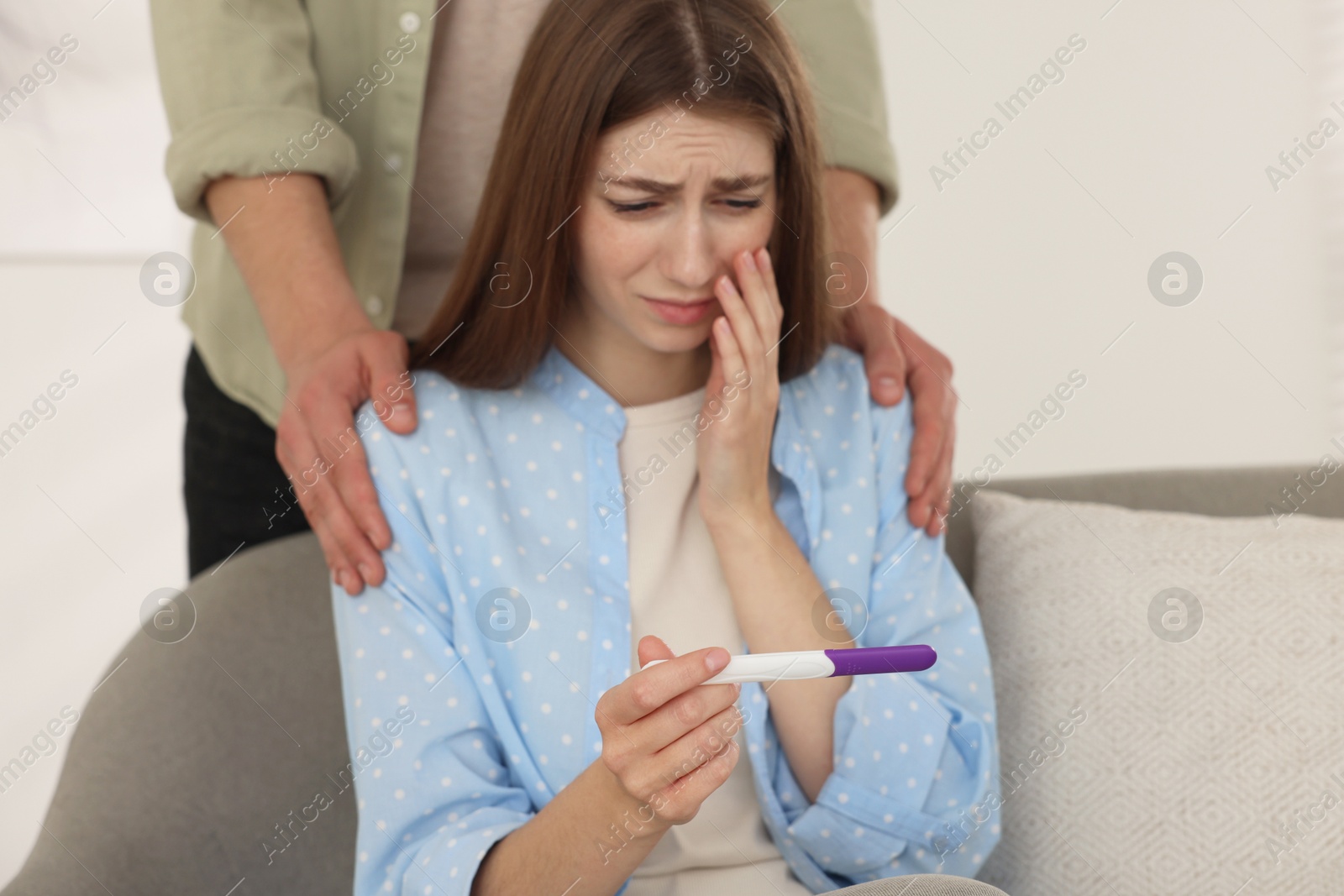 Photo of Upset woman with negative pregnancy test indoors. Man supporting his wife at home