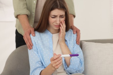 Photo of Upset woman with negative pregnancy test indoors. Man supporting his wife at home