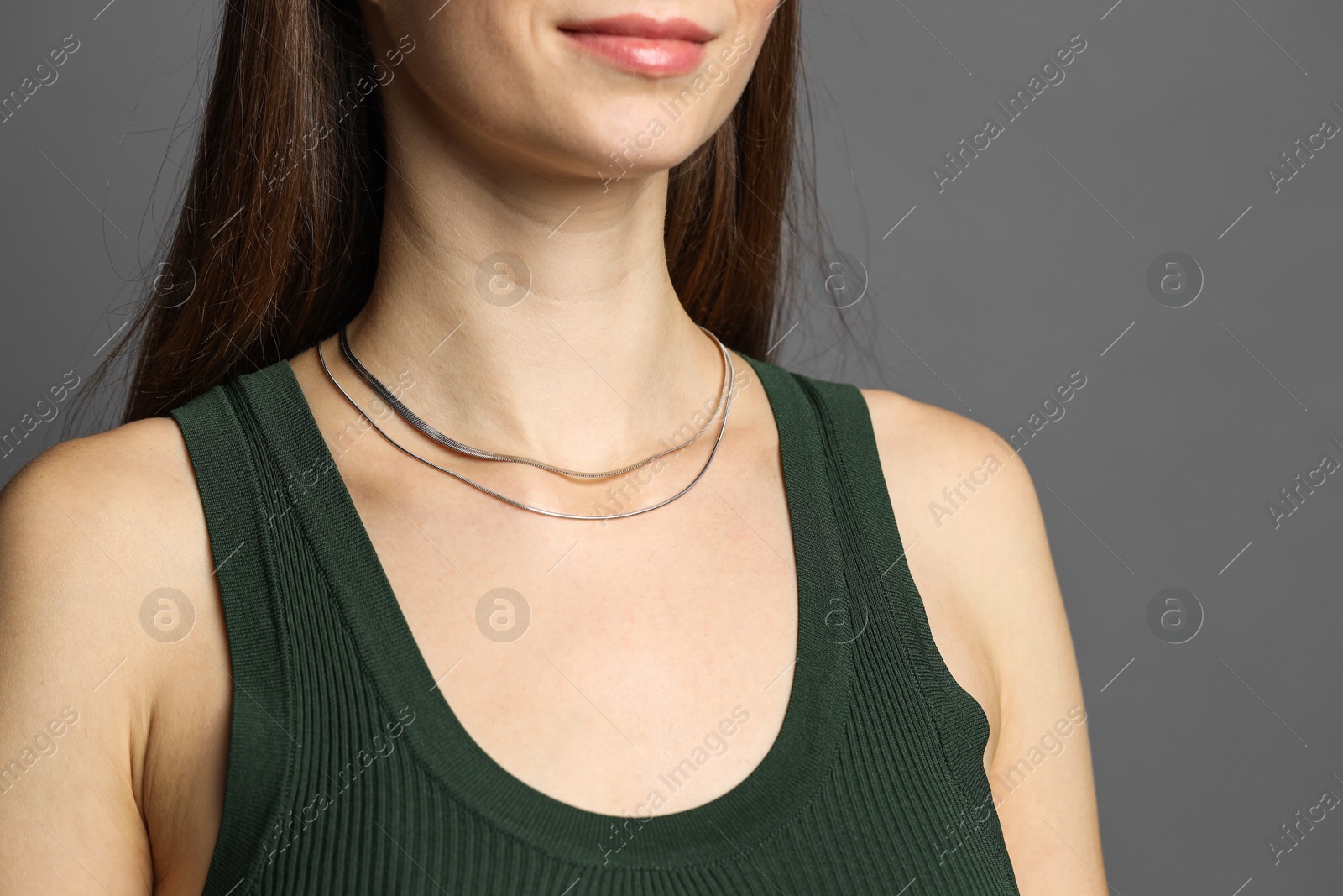 Photo of Woman wearing layered silver necklace on grey background, closeup