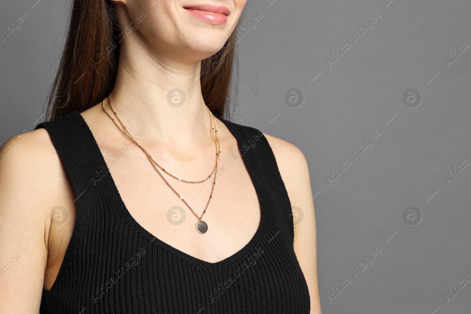 Photo of Woman wearing layered golden necklace on grey background, closeup. Space for text