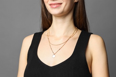 Photo of Woman wearing layered golden necklace on grey background, closeup