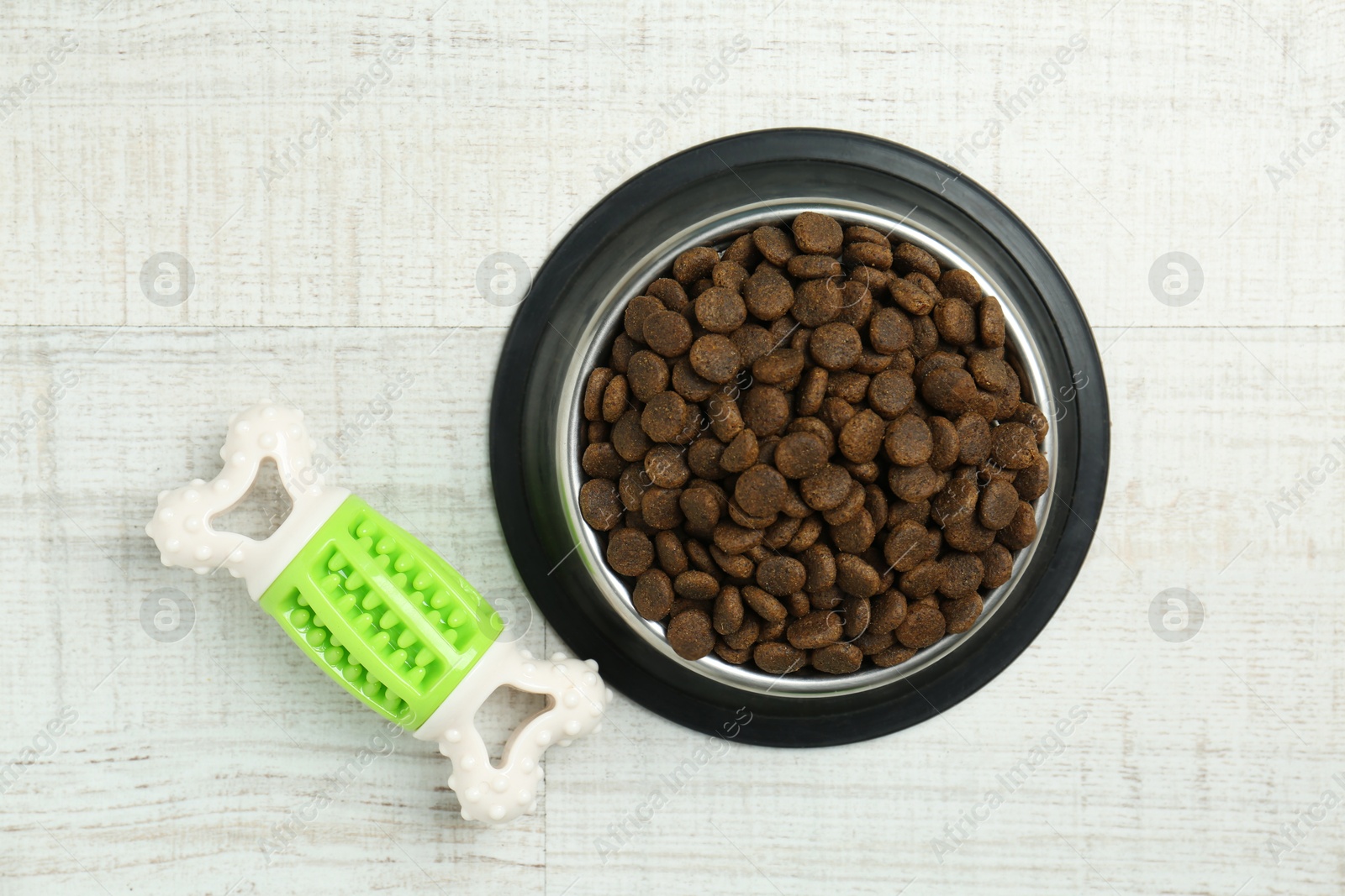 Photo of Dry pet food in feeding bowl and chew bone on floor, top view