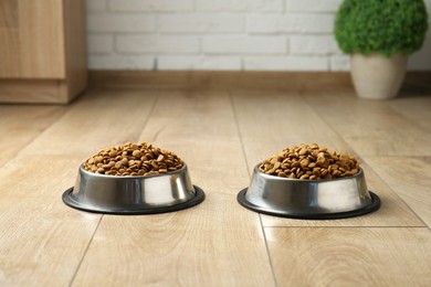 Photo of Dry pet food in feeding bowls on floor indoors