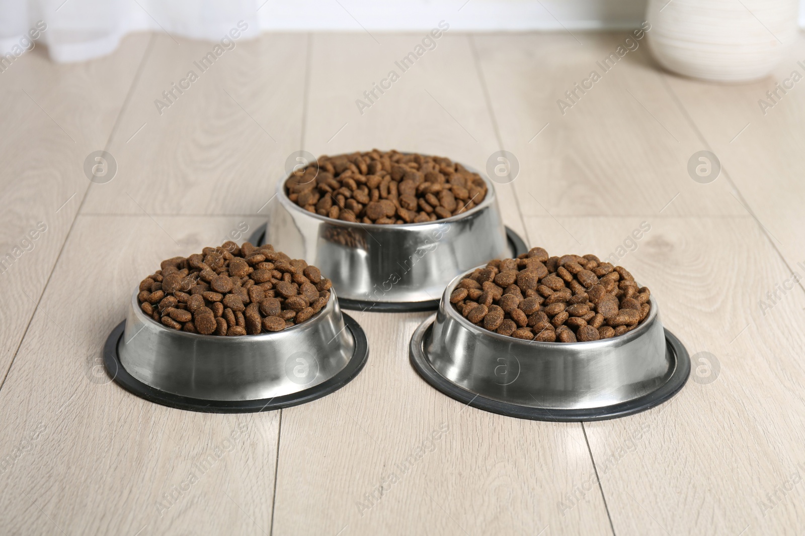 Photo of Dry pet food in feeding bowls on floor indoors