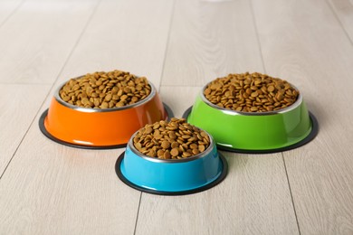 Photo of Dry pet food in feeding bowls on floor indoors