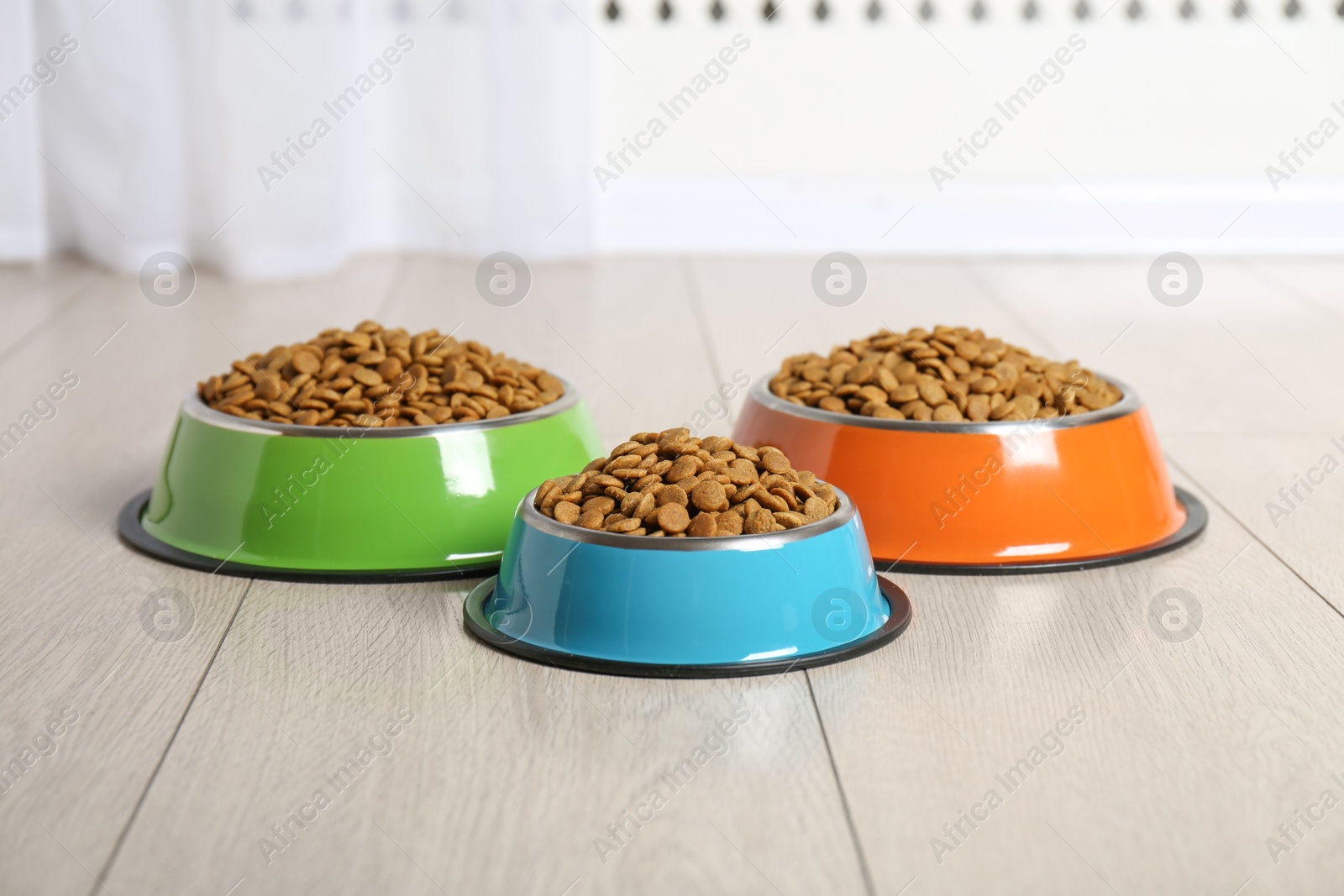 Photo of Dry pet food in feeding bowls on floor indoors