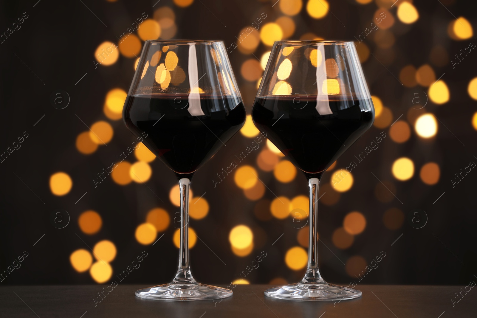 Photo of Tasty red wine in glasses on table against dark background with blurred lights, bokeh effect