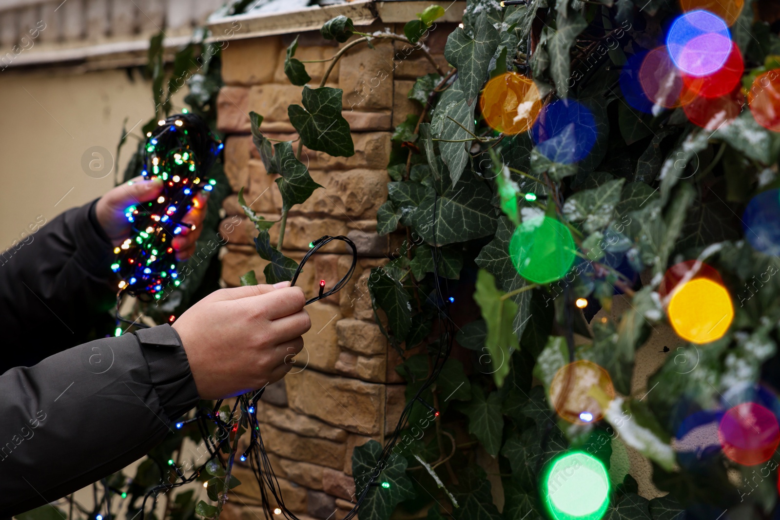 Photo of Man decorating house with Christmas lights outdoors, closeup