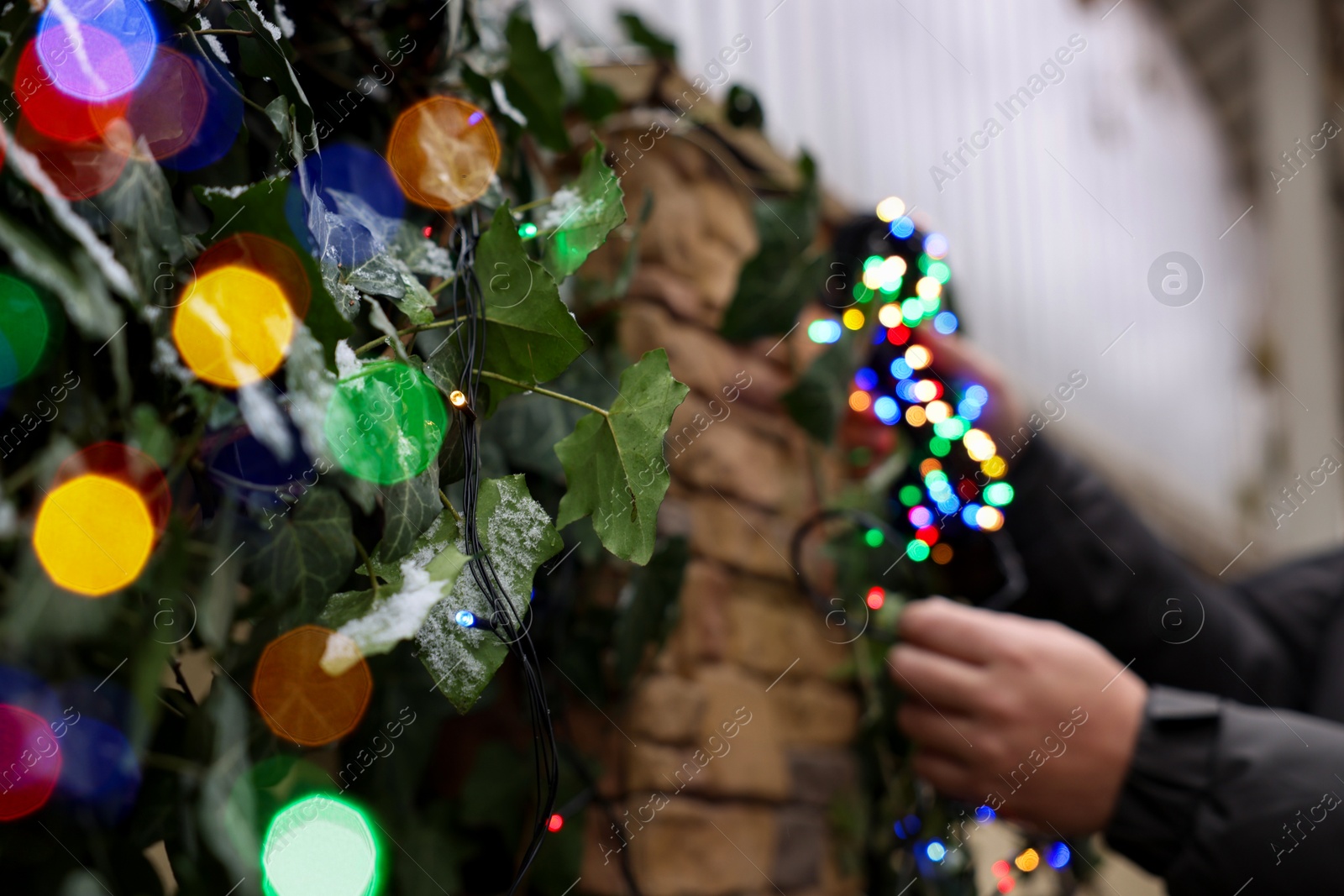 Photo of Man decorating house with Christmas lights outdoors, closeup