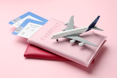 Photo of Travel agency. Flight tickets, passports and plane model on pink background, closeup