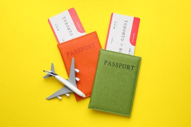 Photo of Travel agency. Flight tickets, passports and plane model on yellow background, top view