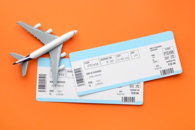 Photo of Travel agency. Flight tickets and plane model on orange background, flat lay