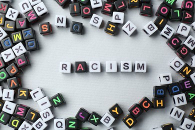 Photo of Word Racism and beads on light grey background, flat lay