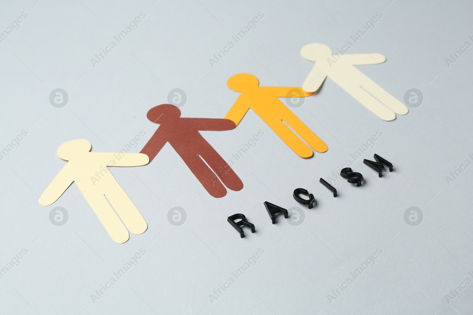 Photo of Word Racism and human paper figures of different colors on light grey background, closeup