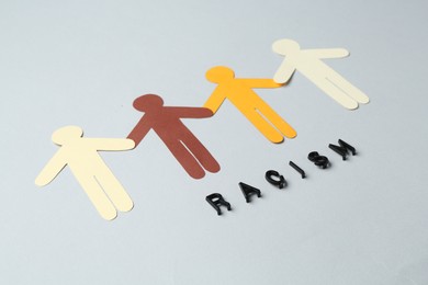 Photo of Word Racism and human paper figures of different colors on light grey background, closeup