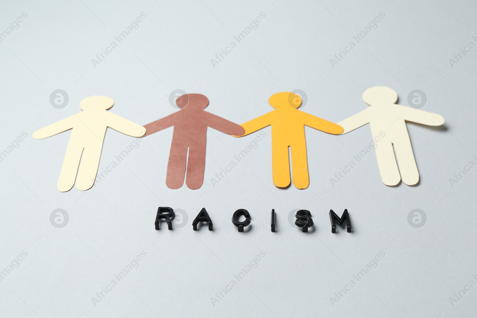 Photo of Word Racism and human paper figures of different colors on light grey background, closeup