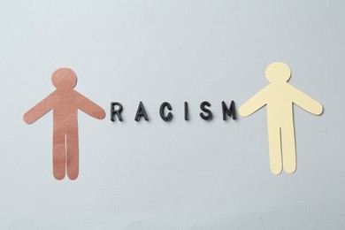 Photo of Word Racism and human paper figures of different colors on light grey background, top view