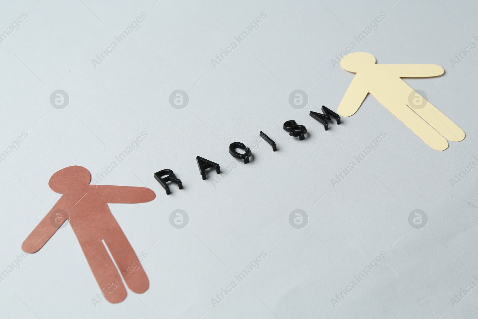 Photo of Word Racism and human paper figures of different colors on light grey background, closeup