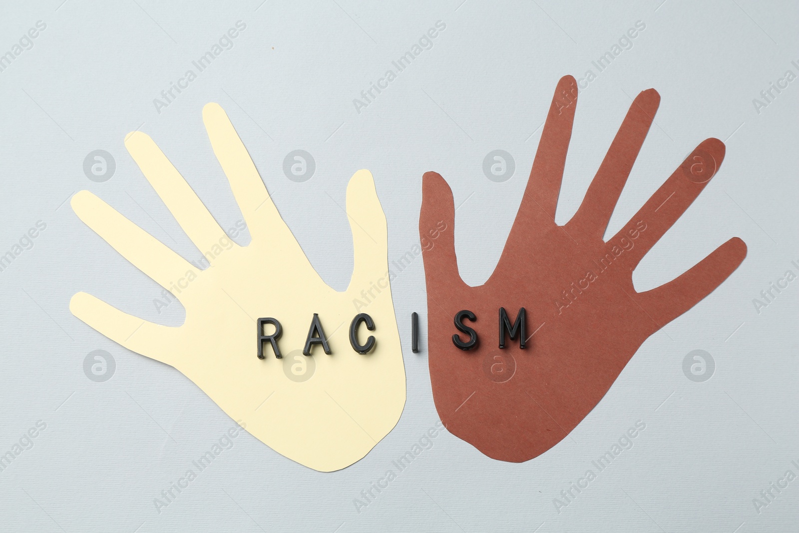 Photo of Word Racism and hands paper figures of different colors on light grey background, top view