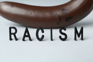 Photo of Word Racism and dark banana with sad face on light grey background, closeup