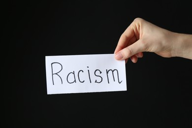 Photo of Woman holding card with word Racism on black background, closeup