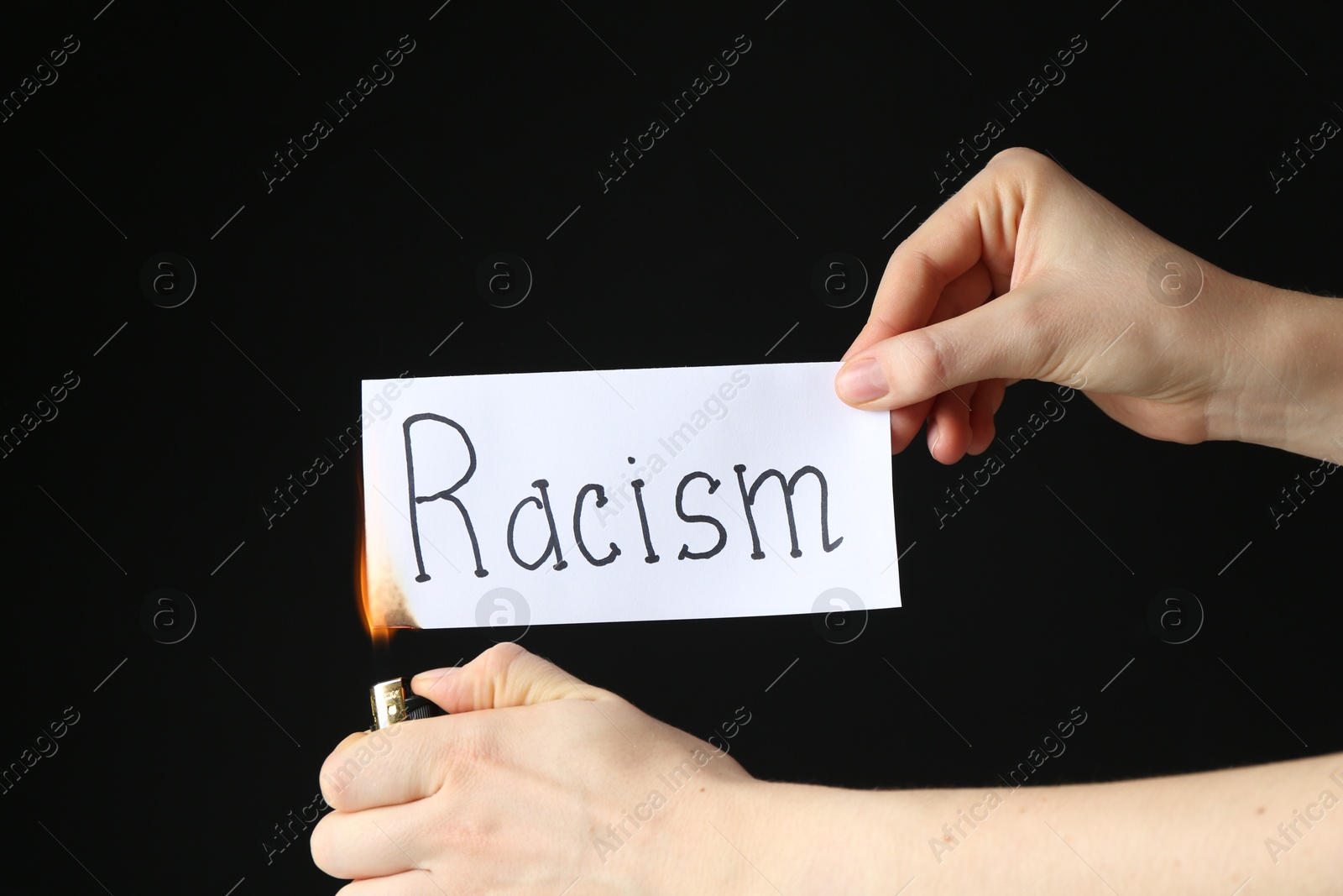 Photo of Woman lighting card with word Racism on black background, closeup