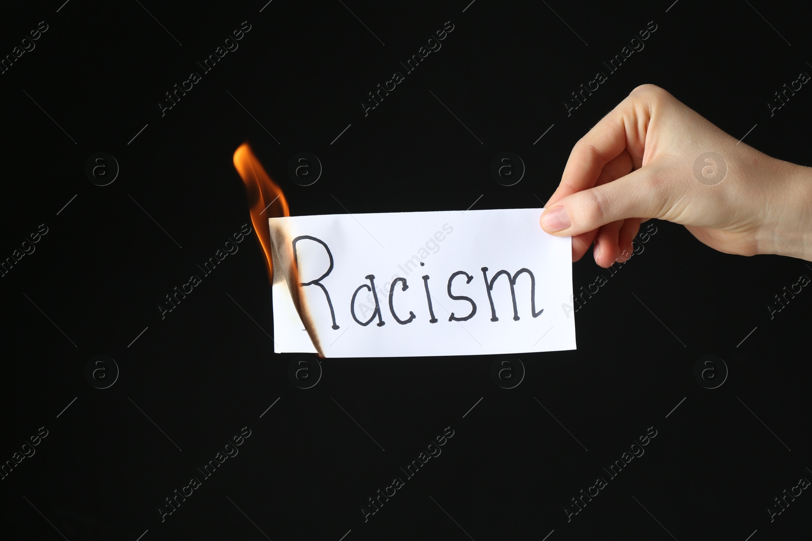 Photo of Woman holding burning card with word Racism on black background, closeup