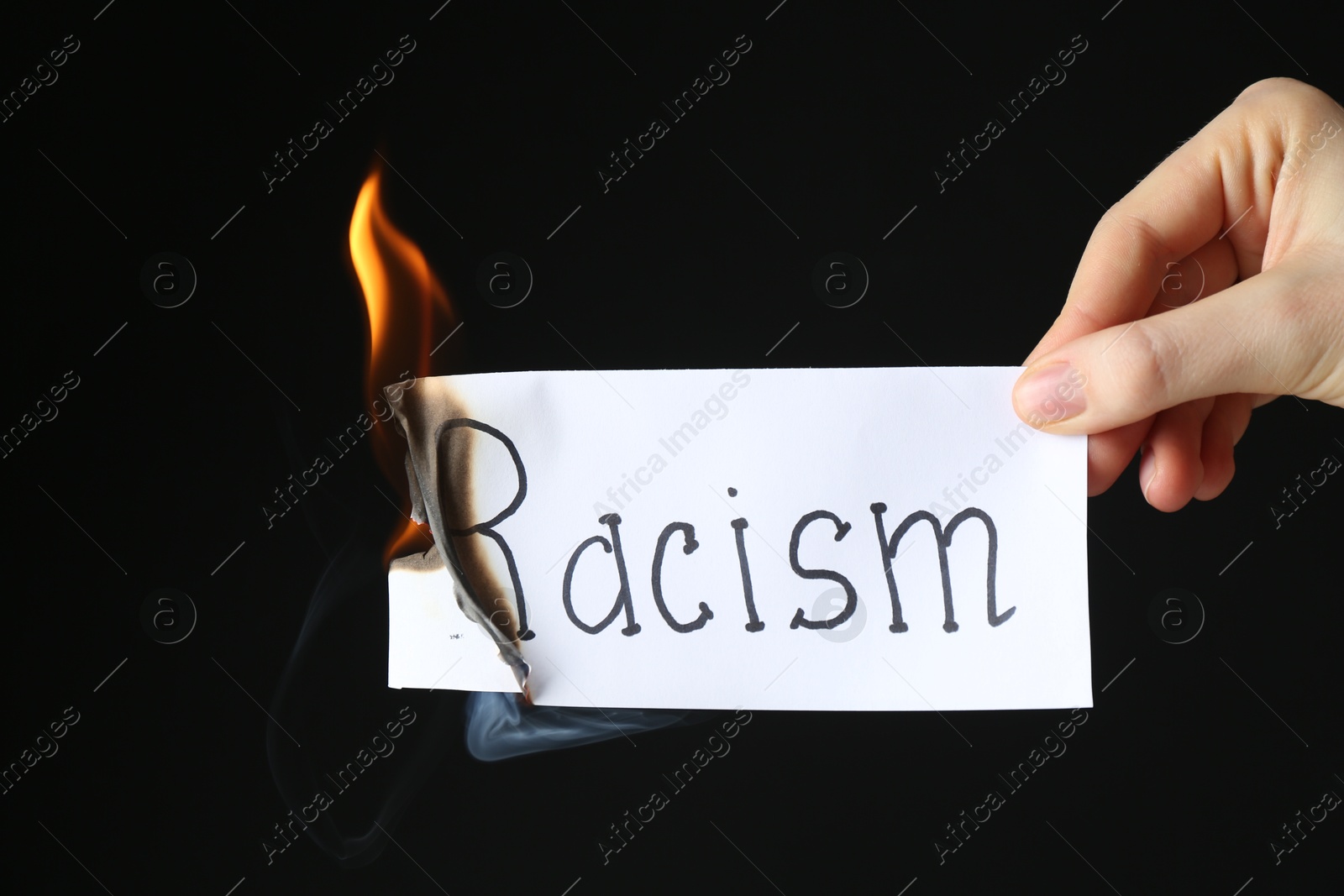 Photo of Woman holding burning card with word Racism on black background, closeup