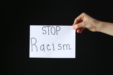 Photo of Woman holding card with phrase Stop Racism on black background, closeup