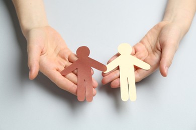 Photo of Stop racism. Woman holding human paper figures of different colors on light grey background, closeup