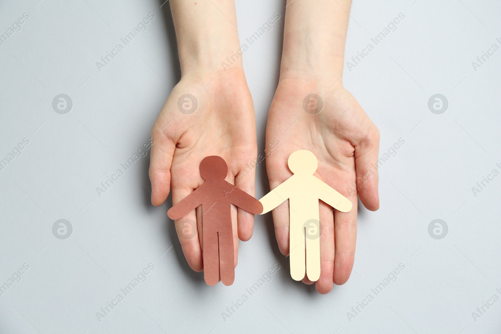 Photo of Stop racism. Woman holding human paper figures of different colors on light grey background, top view