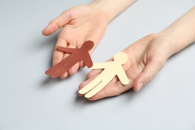 Photo of Stop racism. Woman holding human paper figures of different colors on light grey background, closeup