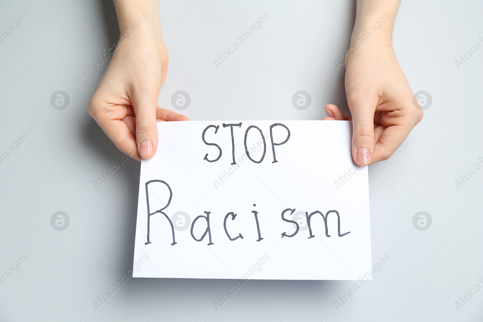 Photo of Woman holding sign with phrase Stop Racism on light grey background, top view