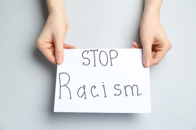 Photo of Woman holding sign with phrase Stop Racism on light grey background, top view