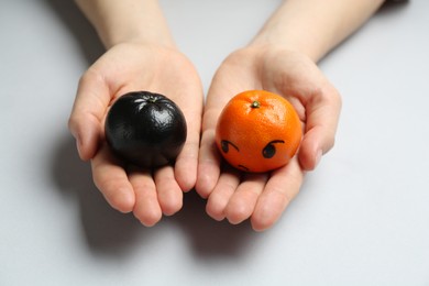 Woman with tangerines of different colors on light grey background, closeup