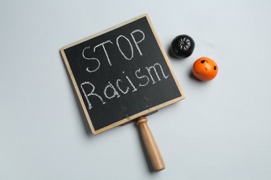 Photo of Chalkboard with phrase Stop Racism and tangerines of different colors on light grey background, top view