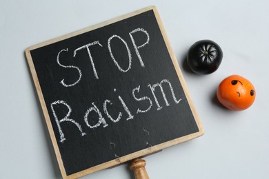 Photo of Chalkboard with phrase Stop Racism and tangerines of different colors on light grey background, top view