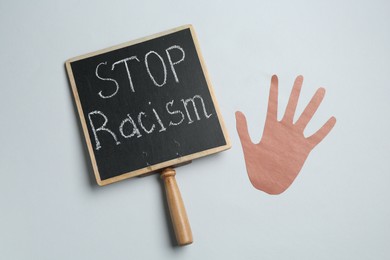 Photo of Chalkboard with phrase Stop Racism and hand paper figure on light grey background, top view