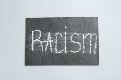 Photo of Chalkboard with word Racism on light grey background, top view