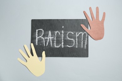 Photo of Chalkboard with word Racism and hands paper figures on light grey background, top view