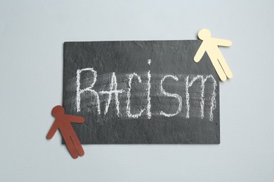 Chalkboard with word Racism and human paper figures on light grey background, top view