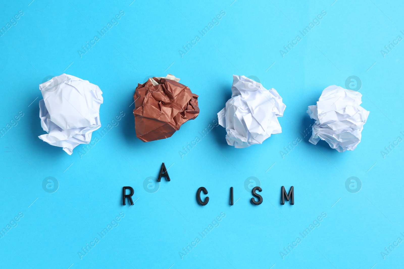 Photo of Word Racism and crumpled paper pieces of different colors on light blue background, flat lay