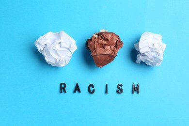 Photo of Word Racism and crumpled paper pieces of different colors on light blue background, flat lay