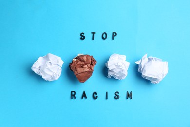 Photo of Phrase Stop Racism and crumpled paper pieces of different colors on light blue background, flat lay