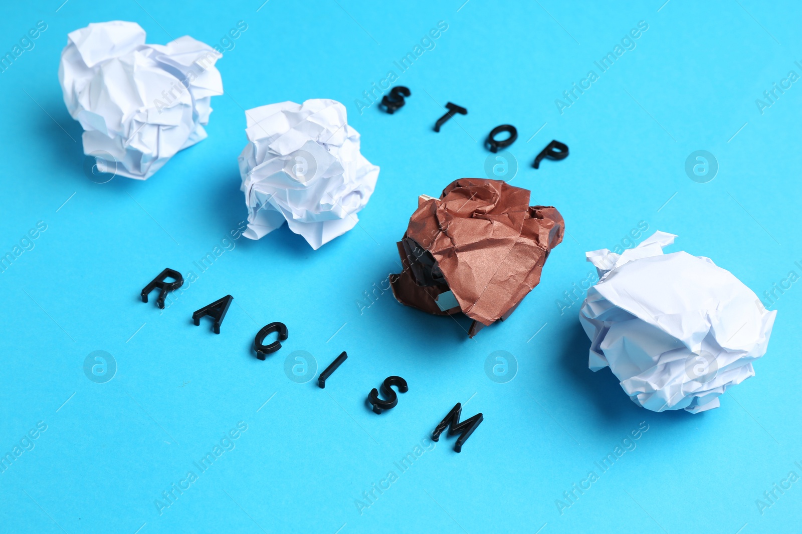 Photo of Phrase Stop Racism and crumpled paper pieces of different colors on light blue background, closeup