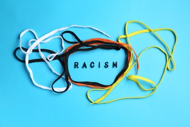 Photo of Word Racism and shoelaces of different colors on light blue background, top view