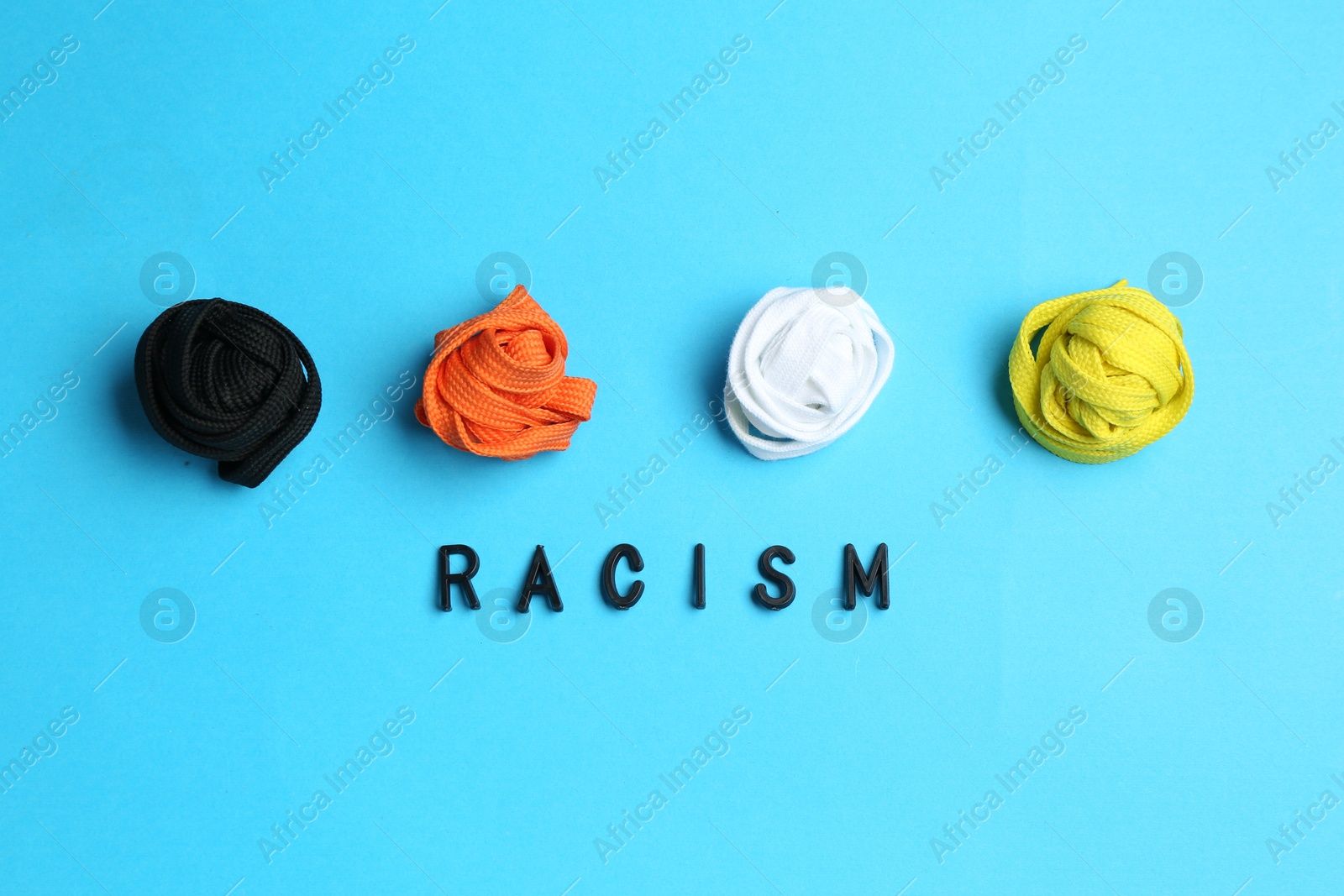 Photo of Word Racism and shoelaces of different colors on light blue background, top view