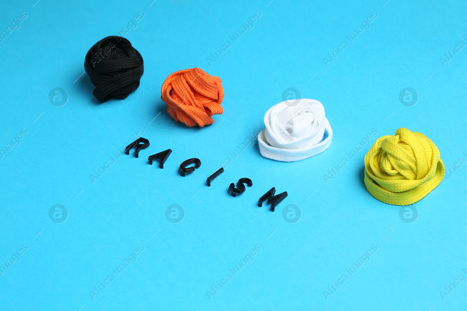 Photo of Word Racism and shoelaces of different colors on light blue background